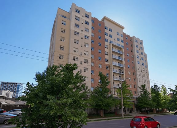 A red car is parked on the street in front of a large apartment building.