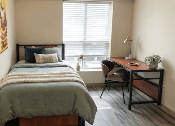 A bedroom with a bed, desk, chair, and window.