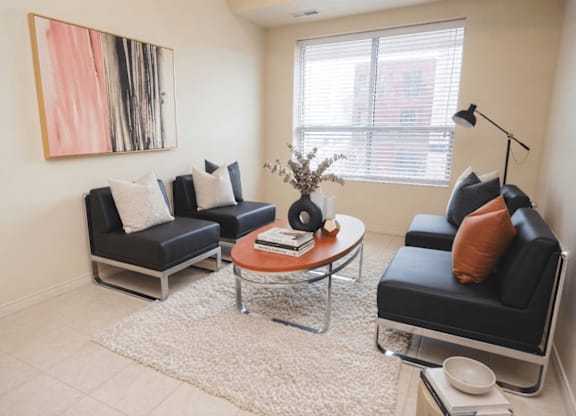 A living room with a black couch, a coffee table, and a painting on the wall.