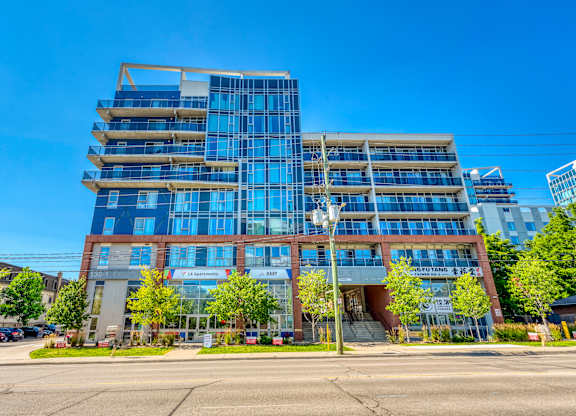 A modern multi-story building with a glass facade and a parking lot in front.