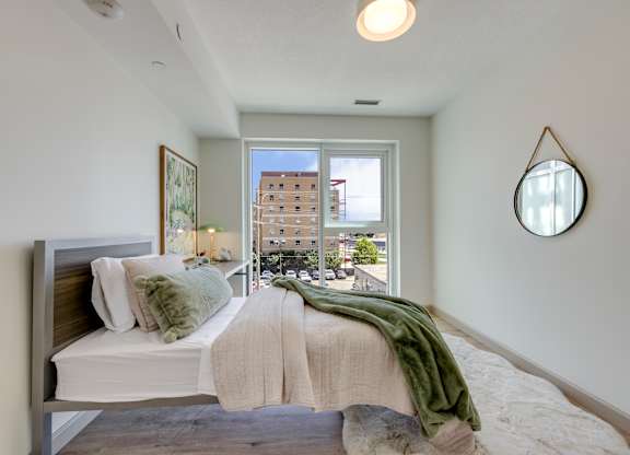 A bedroom with a bed, a mirror, and a window overlooking a city street.