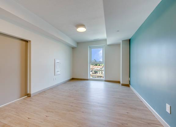 A room with a wooden floor and a window overlooking a balcony.