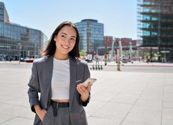A woman in a business suit is standing outside with a smartphone in her hand.