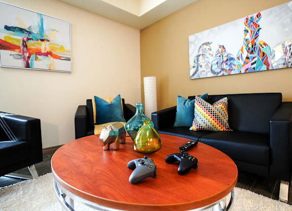 A living room with a black couch, a wooden table, and two gaming controllers on the table.
