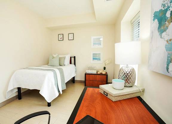 A bedroom with two beds and a nightstand with a lamp.
