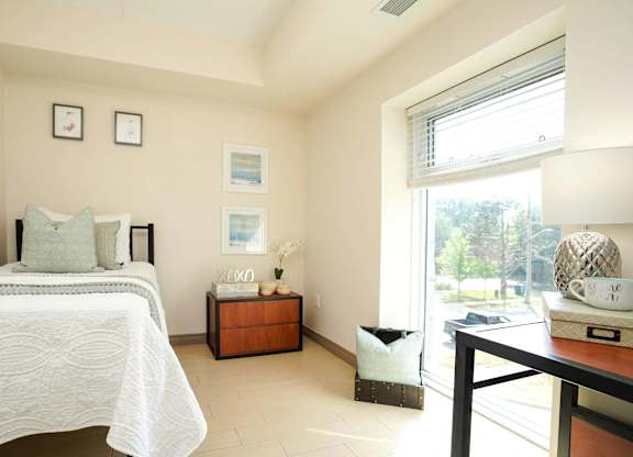 A bedroom with a bed, nightstand, and a table with a lamp.