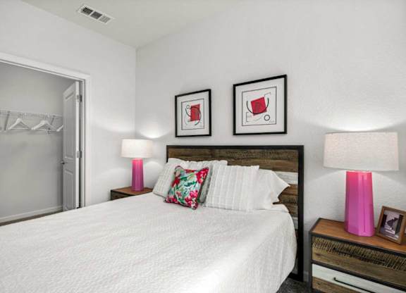 A bedroom with a large bed, two pink lamps, and two framed pictures on the wall.