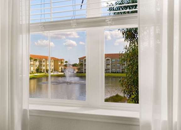 A view of a fountain through a window with white curtains.