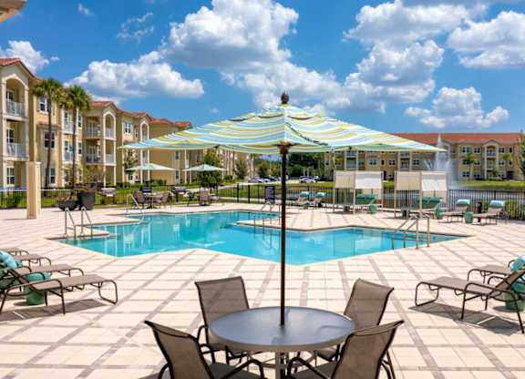 A pool area with a table and chairs and a striped umbrella.