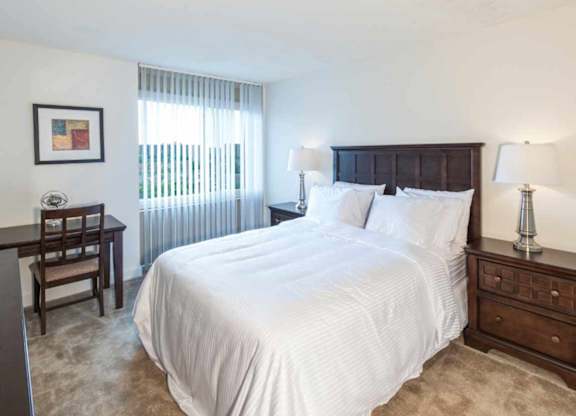 A bedroom with a large bed, a wooden nightstand, and a window with blinds.