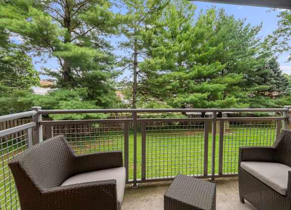 Two chairs and a table on a balcony with trees in the background.