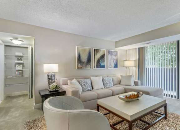 A living room with a white couch, a glass table, and a painting on the wall.