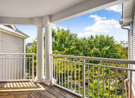the view from the deck of a home with white columns and a view of trees