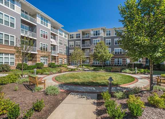 an outdoor area with a fountain and benches in front of an apartment building