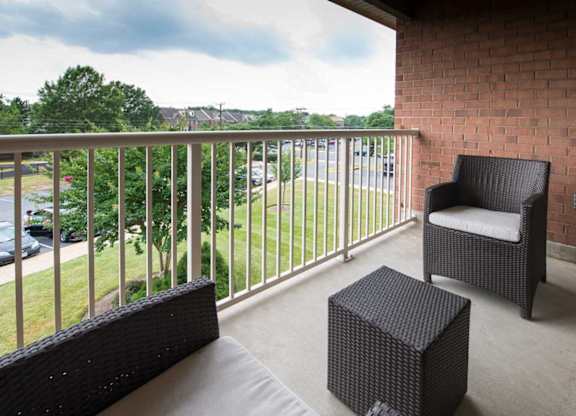 A balcony with a chair and a wicker ottoman.