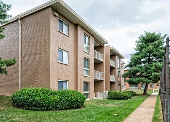 A brown brick apartment building with green bushes in front.