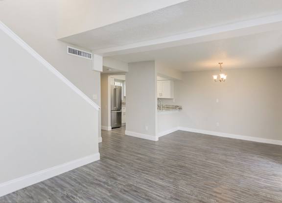 the living room and kitchen of an empty apartment with white walls and wood flooring