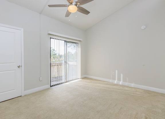 an empty living room with a ceiling fan and a door to a balcony