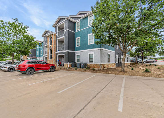 A red car is parked in a parking lot in front of a multi-story building.