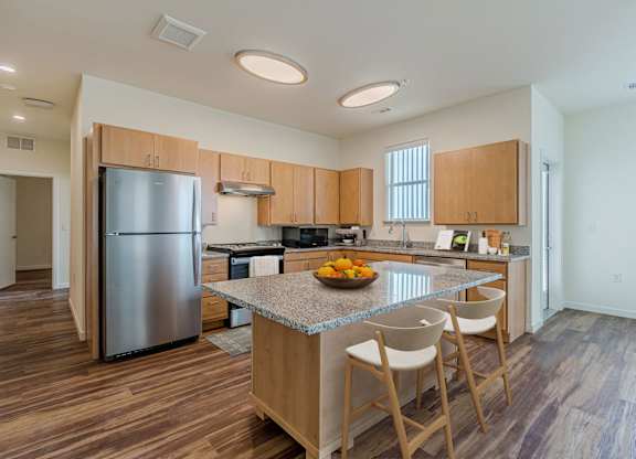 A kitchen with a refrigerator, island, and chairs.