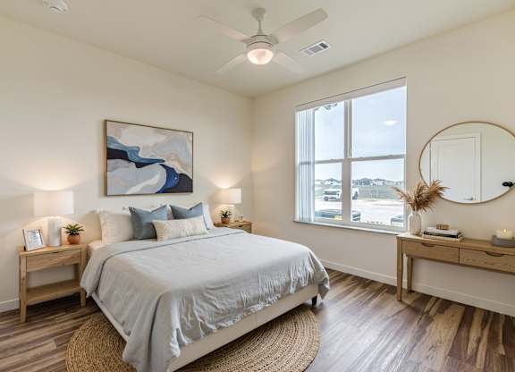 A bedroom with a large bed, a painting on the wall, and a round mirror on the dresser.