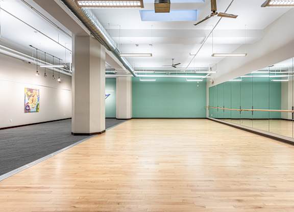 A spacious dance studio with wooden floors and mirrors on the walls.
