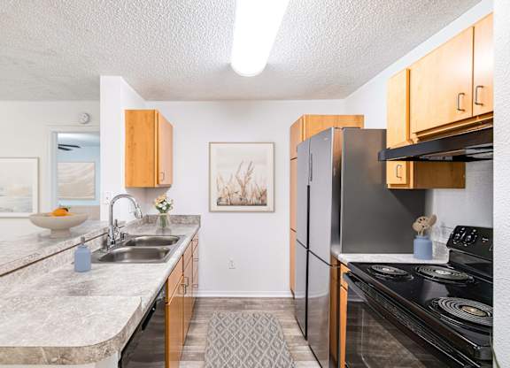 A kitchen with a black refrigerator and a sink with a vase of flowers on the counter.
