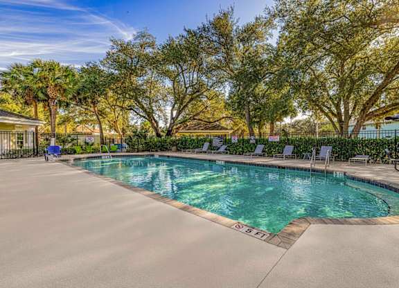 A swimming pool surrounded by trees and lounge chairs.