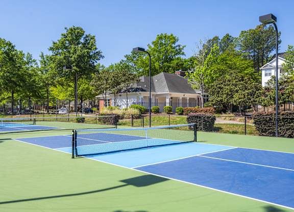 A tennis court surrounded by trees and a building in the background.