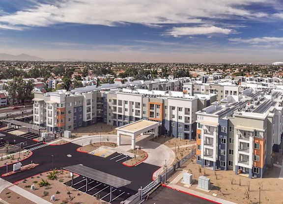 A large, modern apartment complex with a parking lot in the foreground.