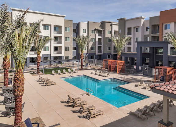 A pool surrounded by palm trees and chairs in front of apartment buildings.
