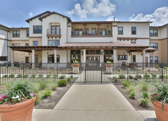 a building with a walkway and a gate in front of it at Cedars of Elk Drive 55+ Apartments, Burleson, 76028