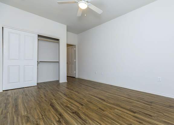 a bedroom with white walls and wood flooring and a closet at Mariposa at Westchester, Grand Prairie, TX