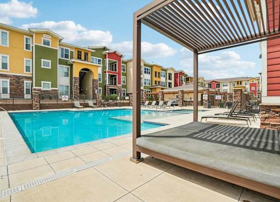 A pool area with a sun lounger and a building in the background.