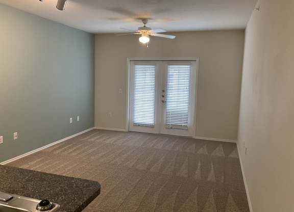 an empty living room with a ceiling fan and a door to a balcony
