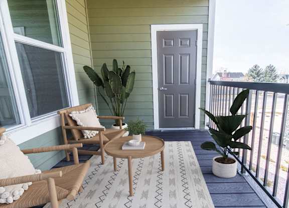 A balcony with a grey door, a cactus, a potted plant, a table and two chairs.