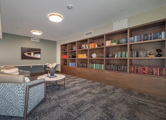 A living room with a grey patterned chair and a coffee table in front of a bookshelf.