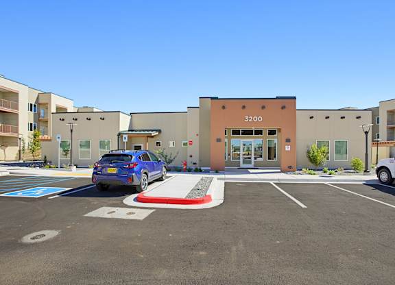 A blue car is parked in a parking lot in front of a building with the number 3200 on it.
