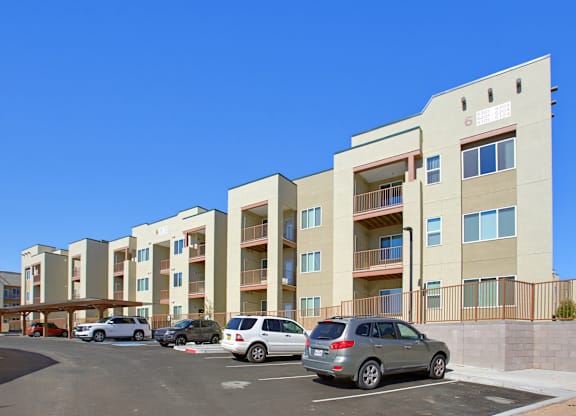 A row of apartment buildings with cars parked in front.
