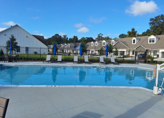 a swimming pool with chairs and umbrellas in front of apartment buildings