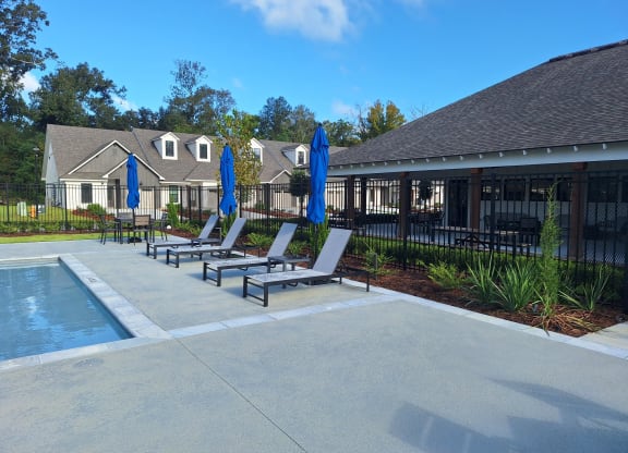 a pool with lounge chairs and umbrellas in front of a house