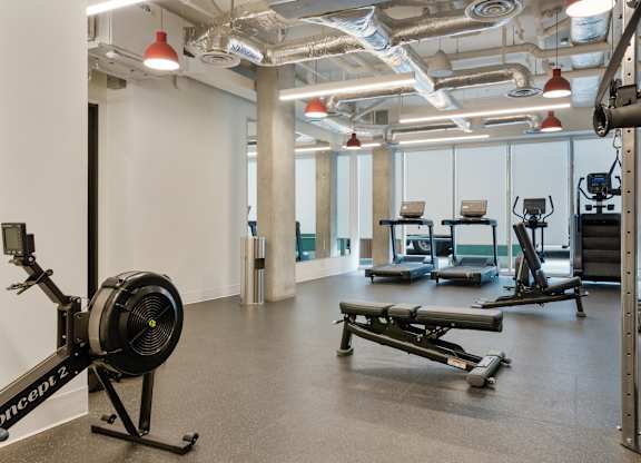 A gym with a rowing machine on the left and a bench press on the right.