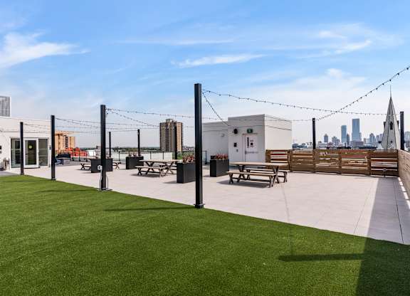 A rooftop patio with a grassy area and picnic tables.