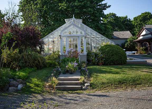 A white greenhouse is surrounded by a gravel driveway and a small garden.