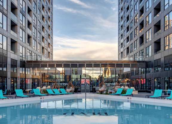 A large indoor swimming pool with lounge chairs is surrounded by two tall buildings.