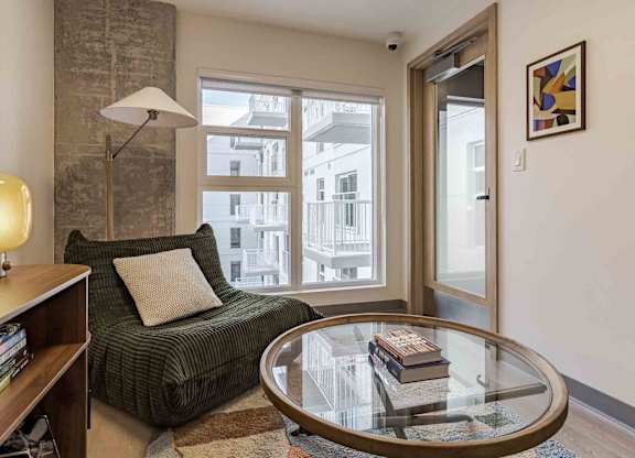 A living room with a green couch, a glass table, and a lamp.