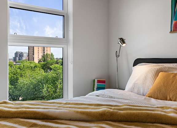 A bedroom with a large window overlooking a cityscape.