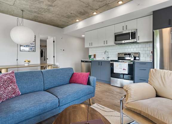 A blue couch with a red pillow sits in a kitchen with a stove and oven.