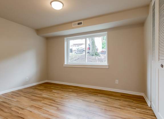 A room with wooden flooring and a window showing a tree and a car outside.