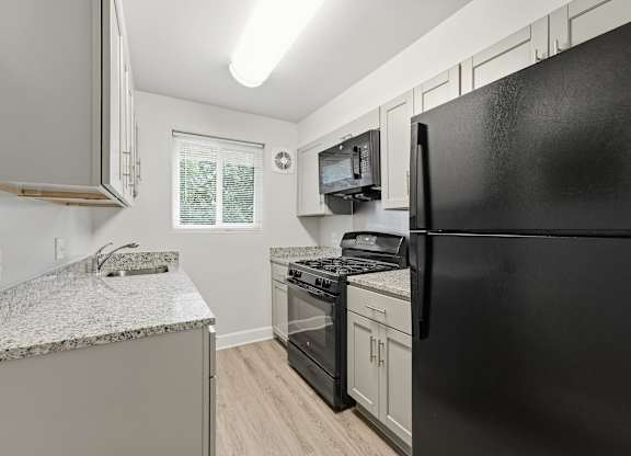 A black refrigerator is in the corner of a kitchen with a granite countertop and stainless steel appliances.